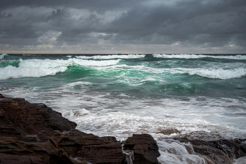 an ocean wave with green colors crashing on rocks