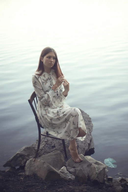 a woman sitting on top of a rock next to a body of water