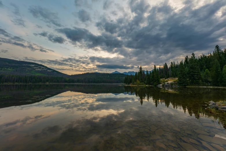 an image of a lake with clouds coming in and sunset in the background