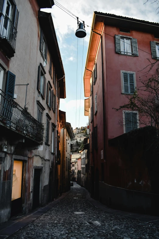 a narrow street with cobblestone pavement and two building that have white shutters