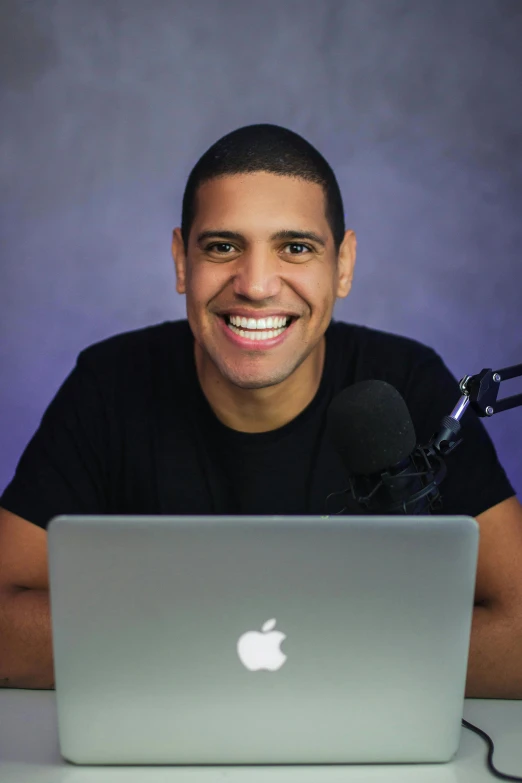 man smiling in front of a silver macbook with a microphone