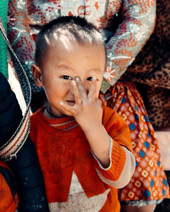 a boy covering his face with one hand standing in front of an indian lady