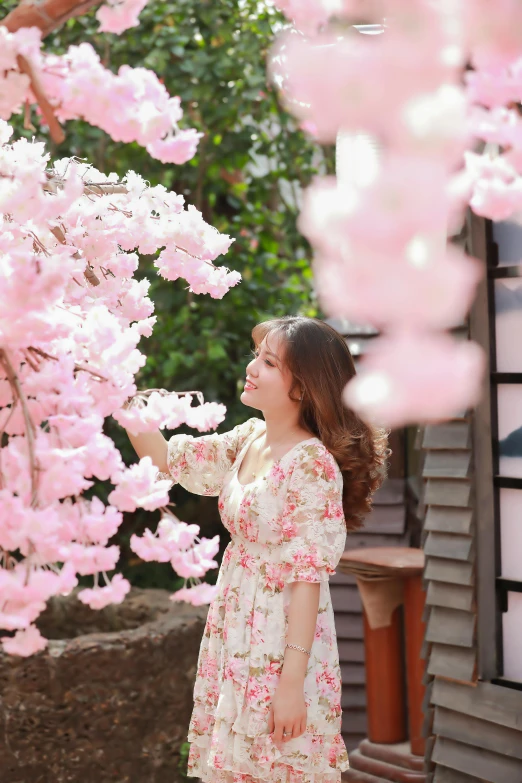 the woman in a pink dress is looking up at some pink blossoms