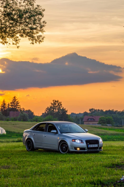 a gray car is parked by itself in the grass at sunset