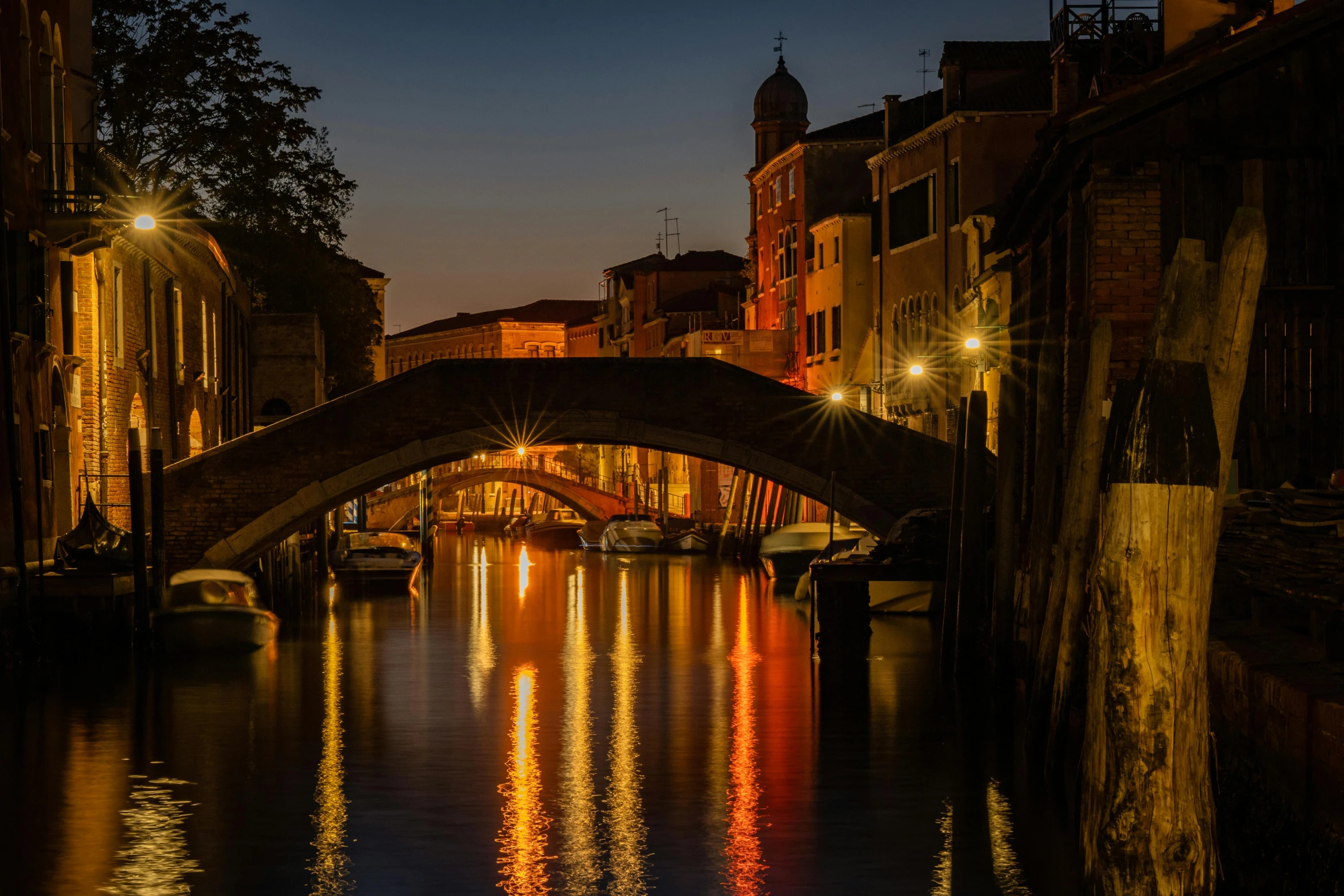 the view of an old bridge across a river with boats below