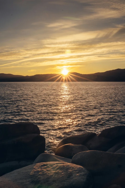 the sun setting on the water by a beach