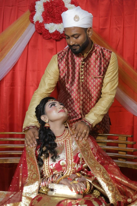 two people dressed in indian clothes standing and sitting