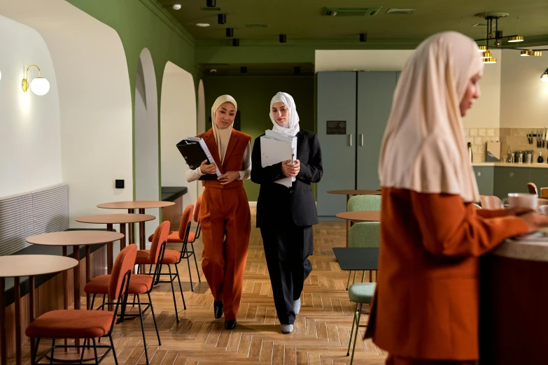 two woman in orange dresses holding papers while walking down a hall