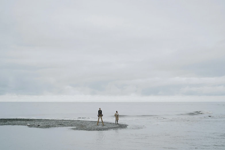 two people are walking in the ocean with a kite flying above them