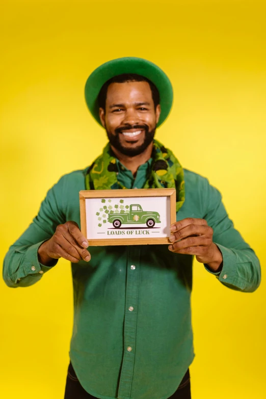 a man wearing a green hat holding up a small framed sign