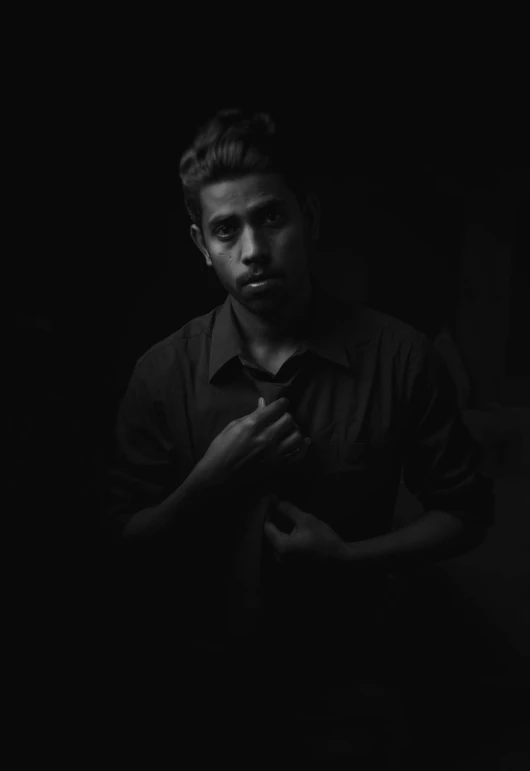 black and white portrait of man standing in dark room with hands crossed