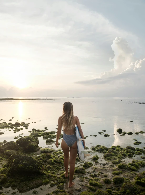 a woman walking along the beach towards the water with her surf board