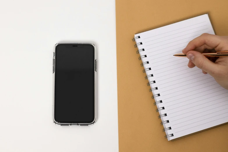 a person using a pen to write on their notepad and holding a cell phone