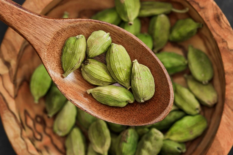 a wooden spoon full of pistachio in front of some other nuts