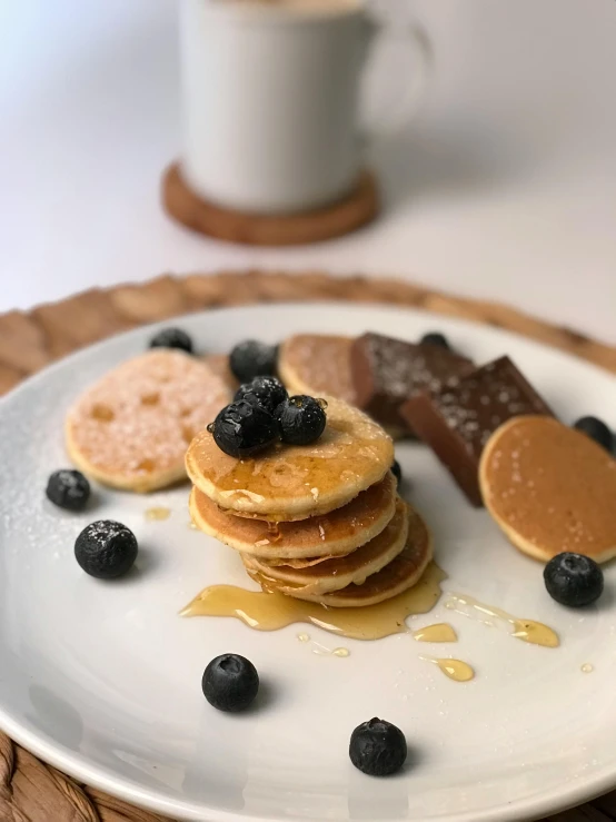 a stack of pancakes on a plate with blueberries and a cup of coffee