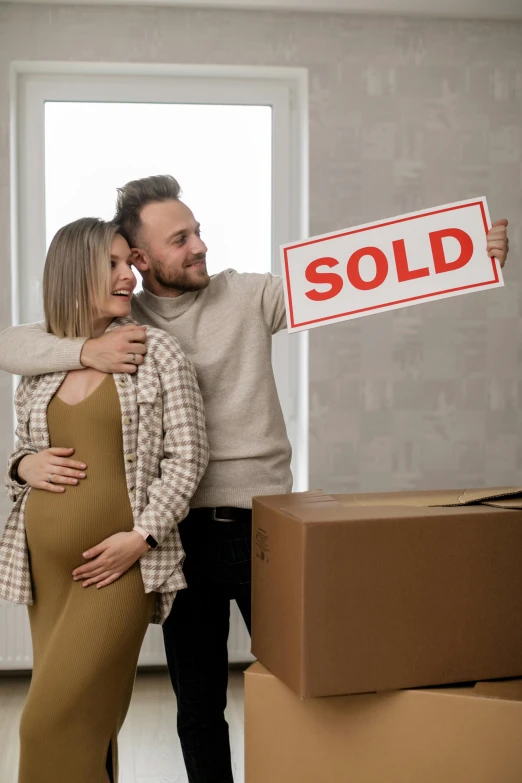 a man and woman posing next to boxes holding a sold sign