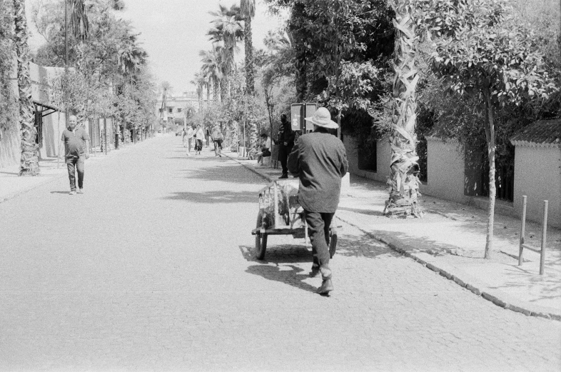 a man in a hat and a backpack rides a cart down a sidewalk