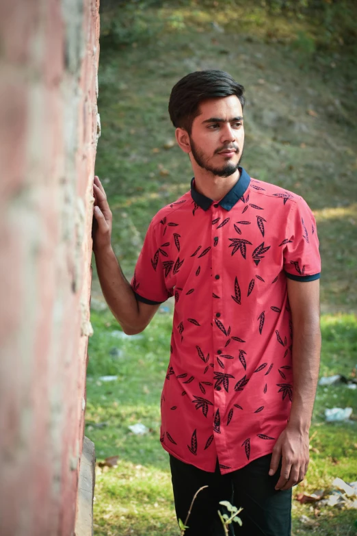 a man in a red shirt leans against a wall