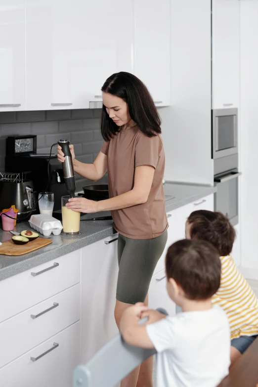 two children sitting at a kitchen counter and an adult standing near by