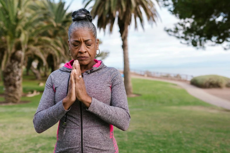 an older woman in yoga gear praying near some palm trees