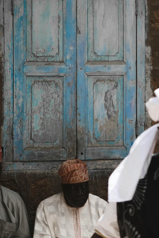 two men sitting down in front of an old blue door