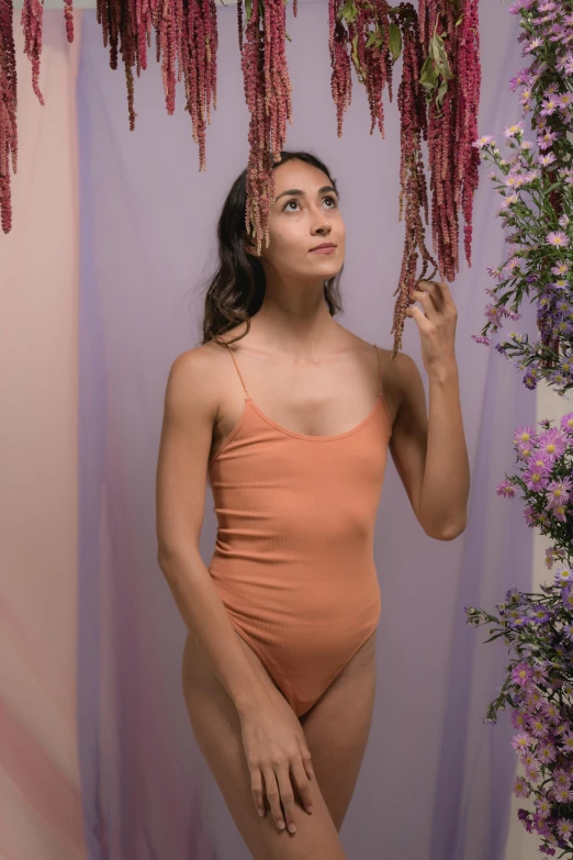 a woman in an orange bodysuit holding flowers and posing