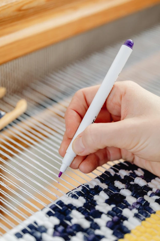 hand holding a pen next to an object that is weaving