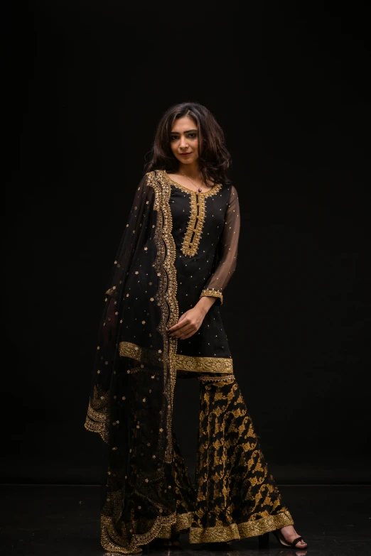 a women in black and gold indian saree standing with hands on hips