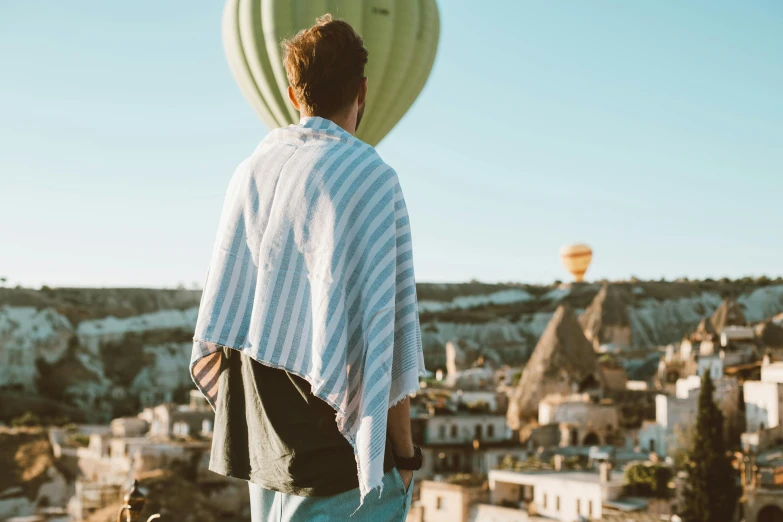 a young man is standing on a hill and looking at the  air balloon