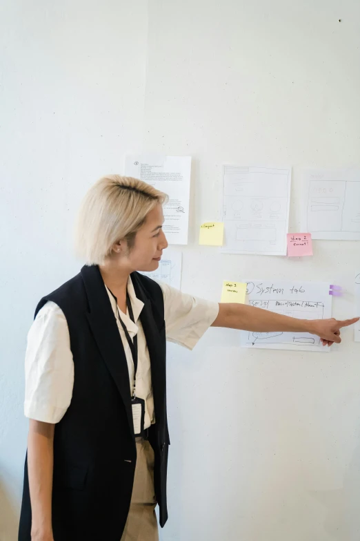 an older woman pointing at sticky notes on a wall