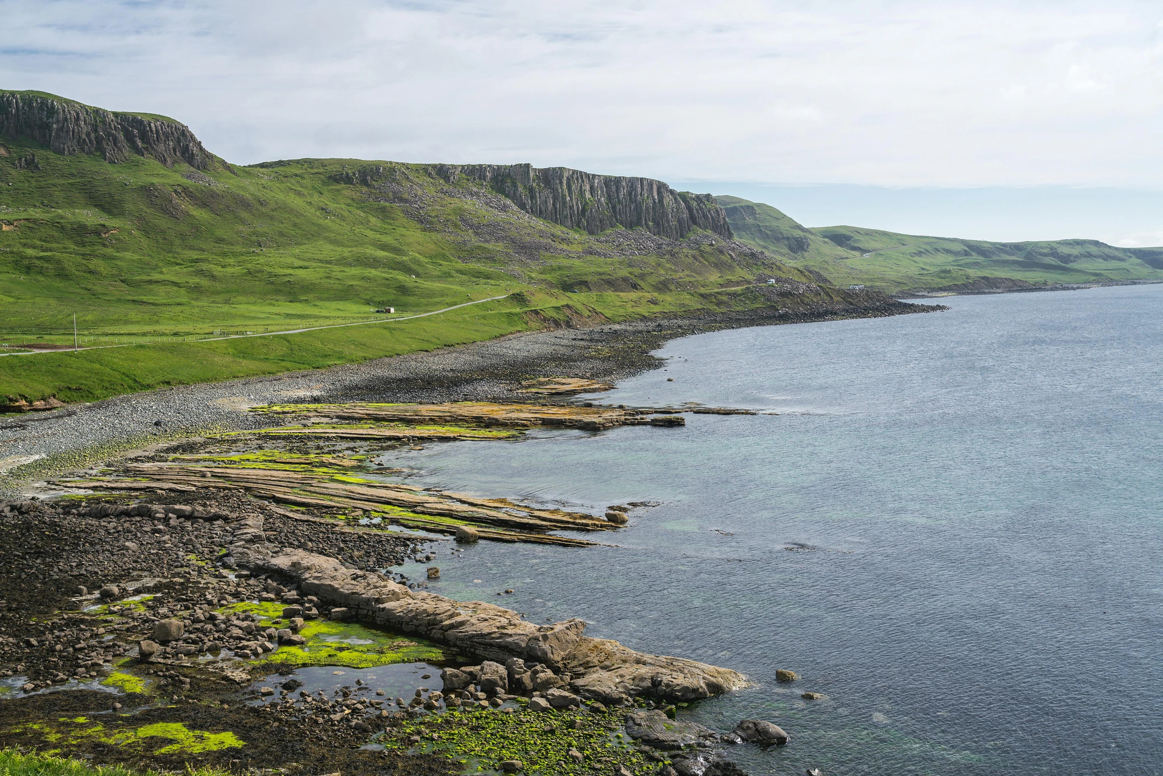 green mountain next to the ocean with grass growing on rocks