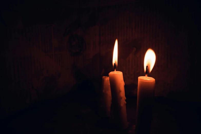 three candles in a dark room lit by candlelights