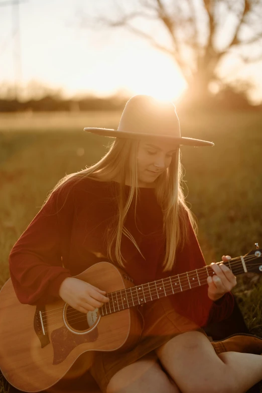 a woman with long hair sitting in a field playing a guitar