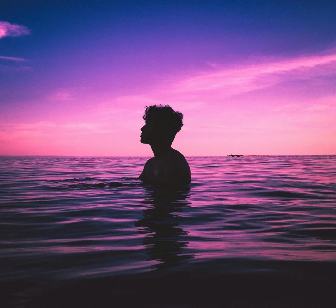 a person floating in the water near a pink sky