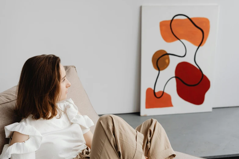 a woman sits in a chair with an orange and white painting behind her