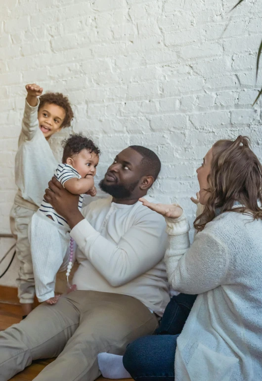 two adults and three children sitting against a white brick wall