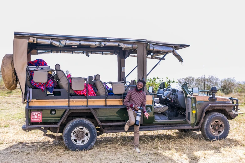 man standing in the cab of an open range jeep with bags strapped to the back