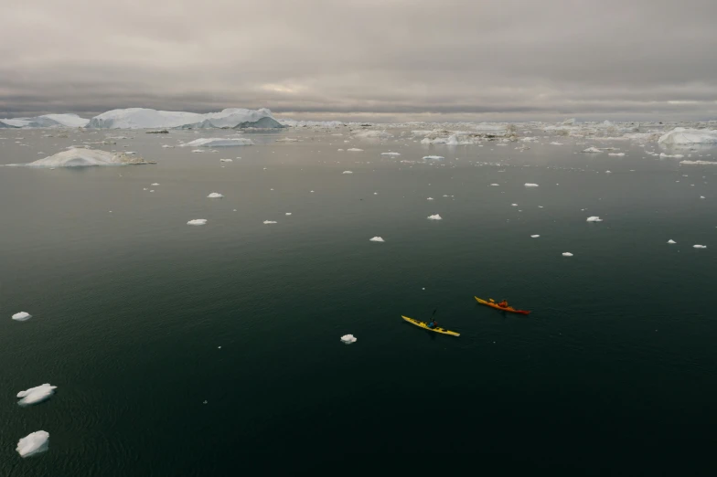 two people paddling in yellow kayaks on the surface of an icy ocean