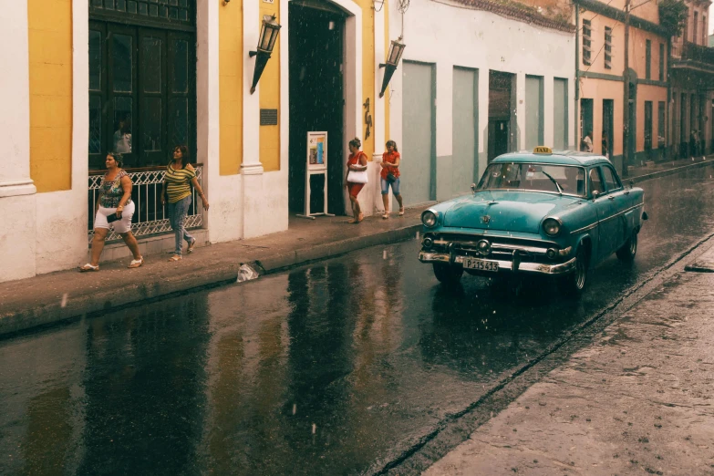 a classic car is parked near the side walk on a rainy day