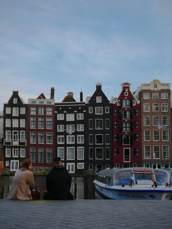 two people sitting on a ledge overlooking a river and many buildings