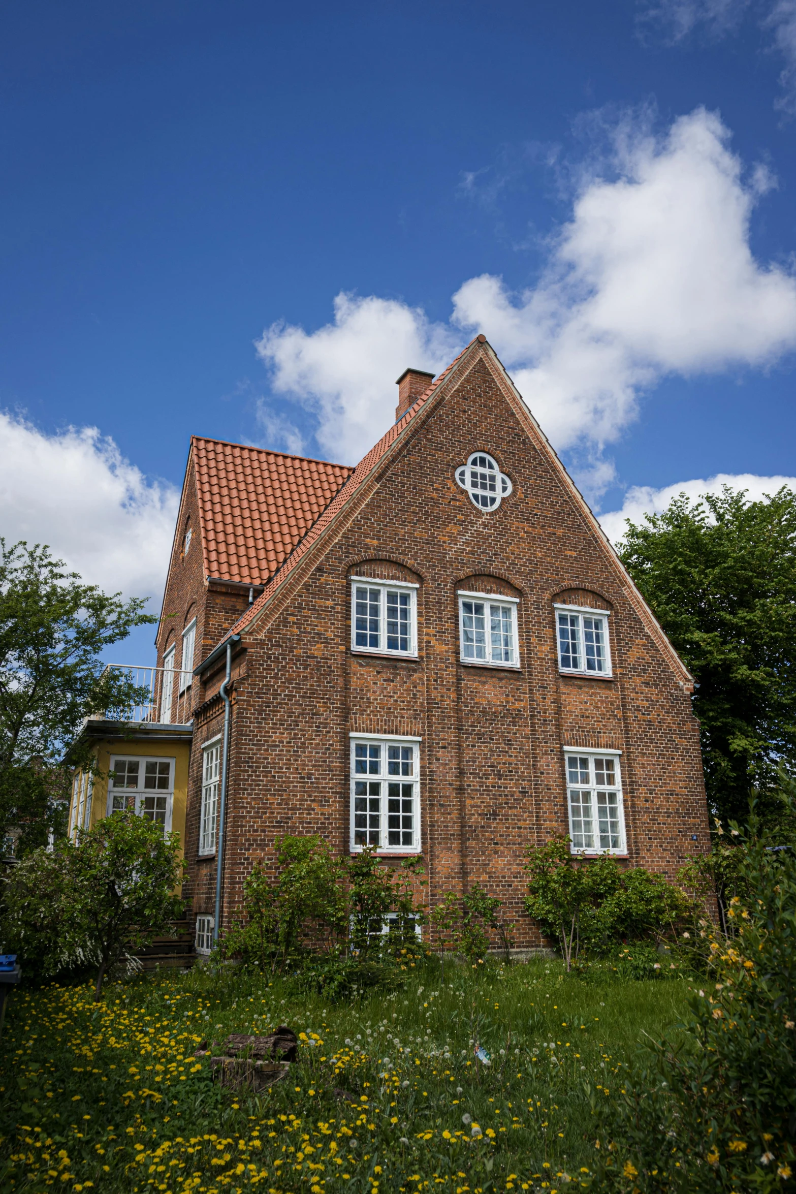 a brown brick house with white windows and a lot of trees around it