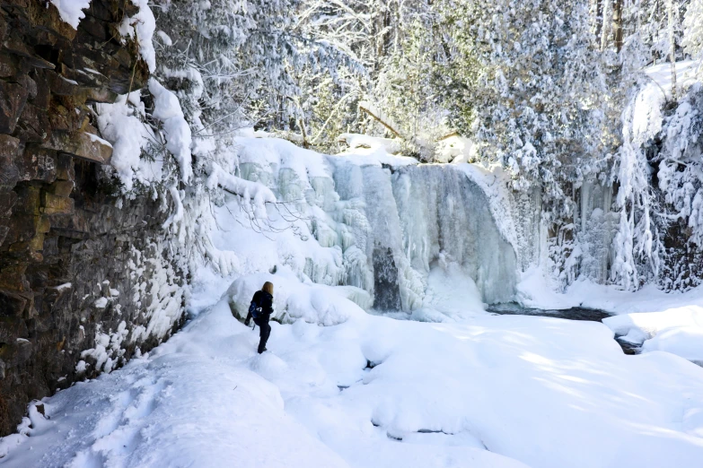 a person is standing in the snow in front of a frozen waterfall