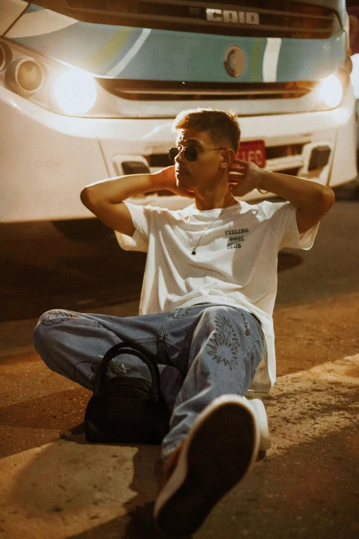 a man sitting on the ground in front of a car talking on his cell phone