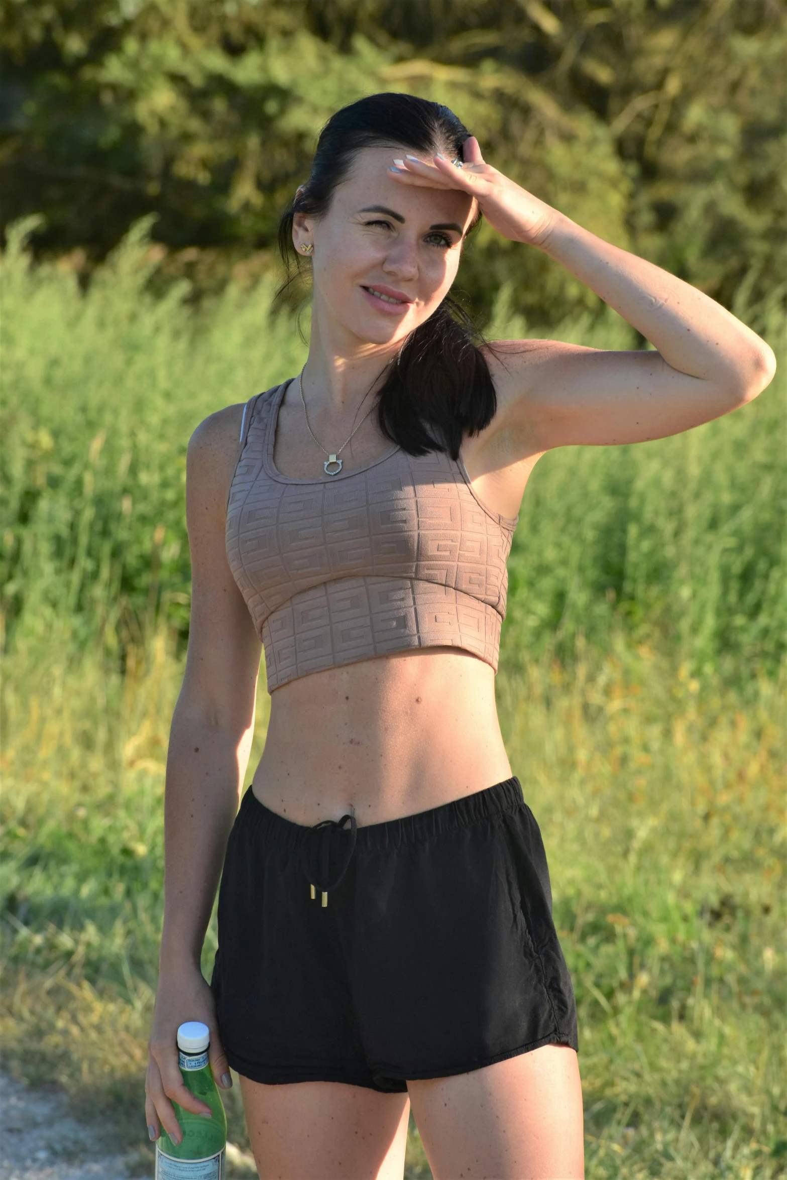 woman wearing a tan tank top standing next to a green field