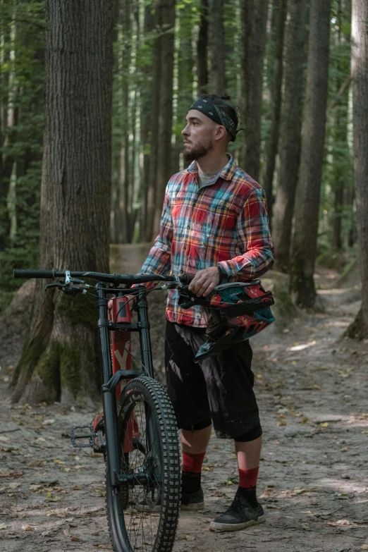 a young man carrying his bicycle in the woods