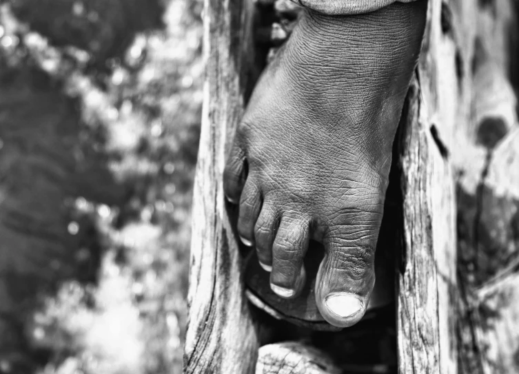 the bare foot of a man standing near a wooden post