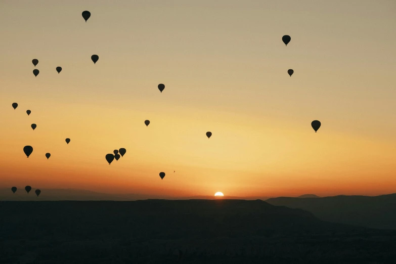 many balloons flying at dusk on the horizon
