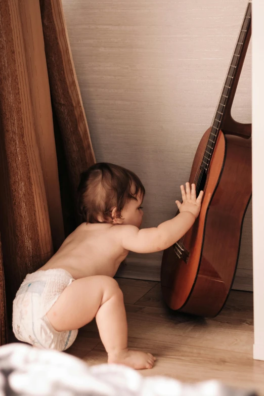 a baby in diapers reaching at a guitar