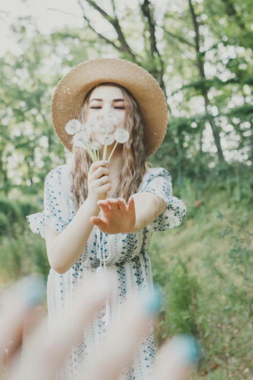 a woman wearing a hat blowing a dandelion