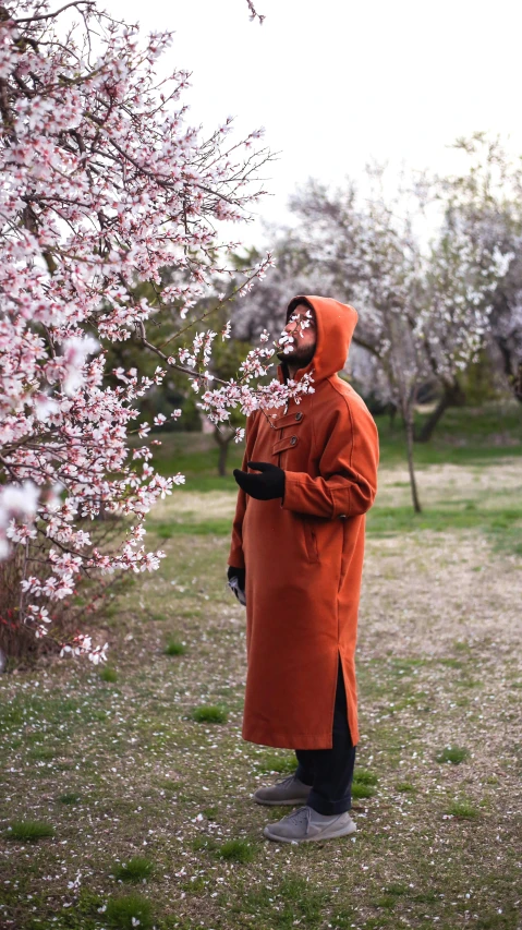 man with hooded jacket and cap standing next to blooming tree